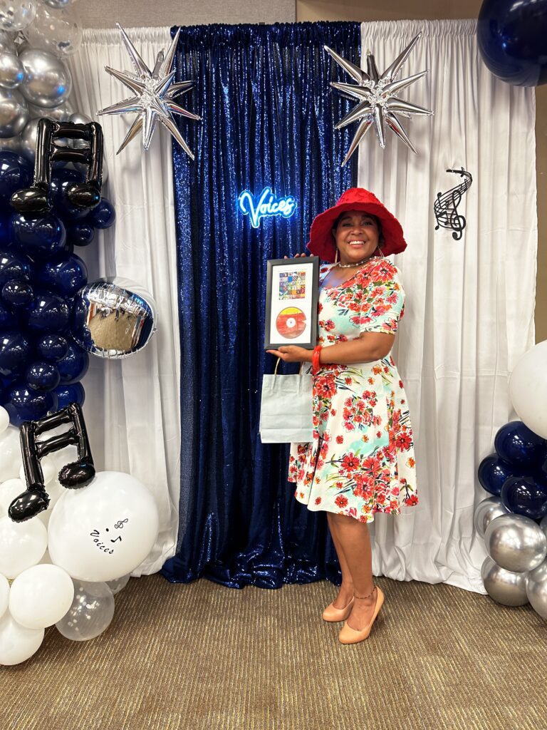 Voice album contributor poses at Voices photobooth with a plaque containing a CD and the album cover