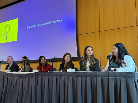 Six people sit on a panel in front of a large screen