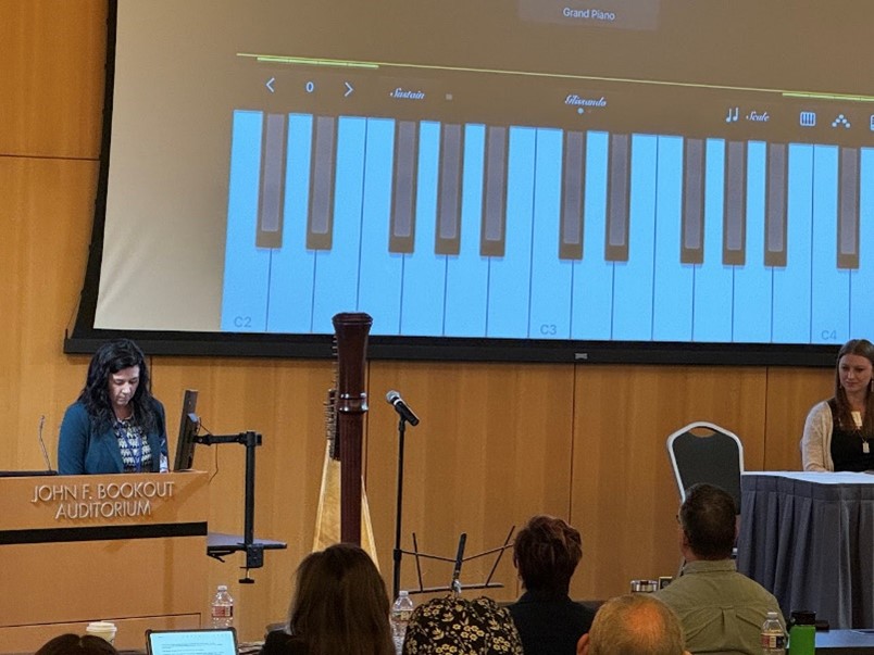 Music therapist Mary Kate Becnel presents in front of a large screen with a keyboard