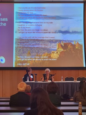 Jennifer Townsend and Suzanne Hanser sitting in front of a large screen with lyrics