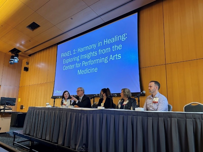 Five people sit on a panel in front of a large screen